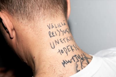 Miehen niska, johon tatuoitu teksti "Välillä reissussa unetkin todeksi muuttuu".