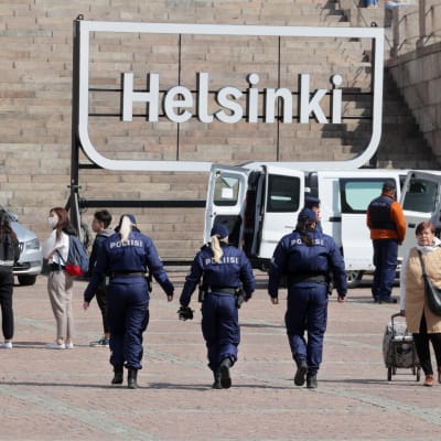 Kolme poliisia kävelee poispäin. Taustalla on Helsinki -kyltti.