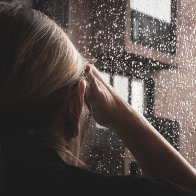 Nainen katselee sateisesta ikkunasta ulos.