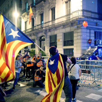 Man invirad i katalansk flagga kastar orangefärgad plastboll mot polis.