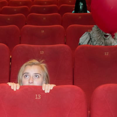En ung kvinna kryper ihop bakom biografstolen, bakom henne syns olika monster från skräckfilmer.