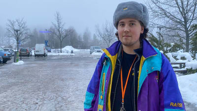 En ung man i pälsmössa står på en isig gårdsplan.