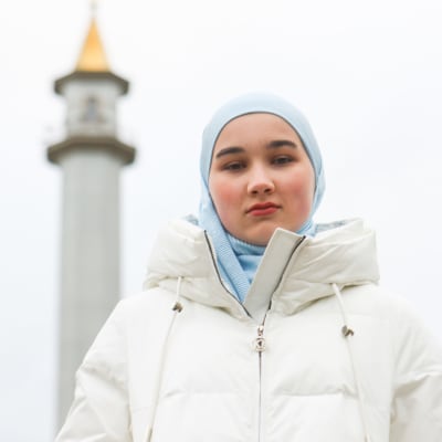 Hijabia käyttävä Asija Alejeva, taustalla moskeijan minareetti.