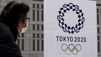 Person med ansiktsmask tittar på plakat med OS-logon.