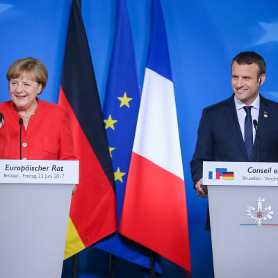 Tysklands förbundskansler Angela Merkel och Frankrikes president Emmanuel Macron ler bakom sina podium med Tysklands, EU:s och Frankrikes flagga i bakrgunden på EU-toppmötet.