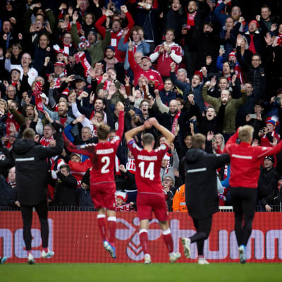 En läktare full av euforiska fans i rödvitt får hälsningar av spelarna efter en match.