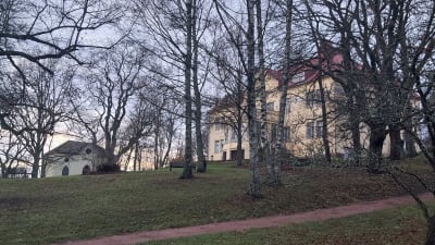 Gräddgul herrgård i en trädgård på hösten.