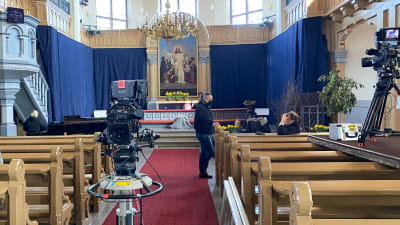 Bild mot altaret i en kyrka. Flera personer och flera filmkameror syns.
