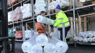 Två män lastar stora rullar med plast på en truck.