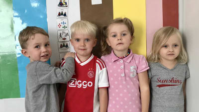 Fyra barn i dagisåldern står framför en färgglad planch.
