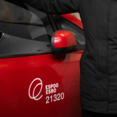 En person står invid en röd bil, med Esbos logotyp.