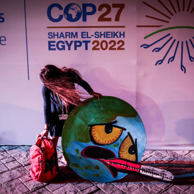Klimataktivist med en pappfigur som förestället ett ledsam jordklot med en febertermometer i munnen. 