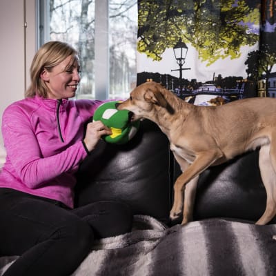 En kvinna sitter i en soffa och leker med en hund.
