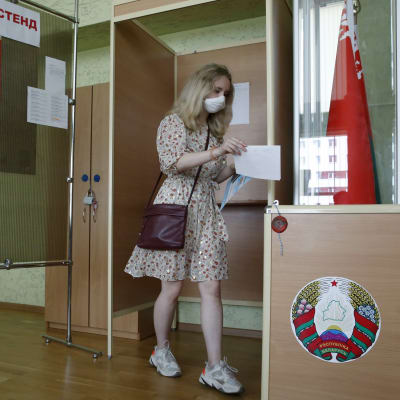 En ung kvinna med munskydd lägger sin röst i en valurna. Hon förhandsröstar i presidentvalet i Belarus.