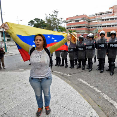 En demonstrant håller Venezuelas flagga framför en rad kravallpoliser