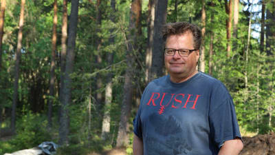 Man i glasögon med blå t-tröja med tryck poserar i en skogsglänta