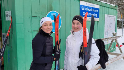 Två kvinnor med skidor i händerna.
