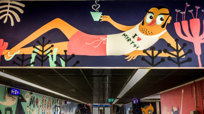 Myyrmäen juna-asemalla seinämaalaus, jossa loikoilee mieshahmo, jolla paita jossa teksti I love Myrtsi.