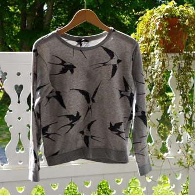 En grå tröja med fågelmönster. Tröjan hänger på tork utomhus.