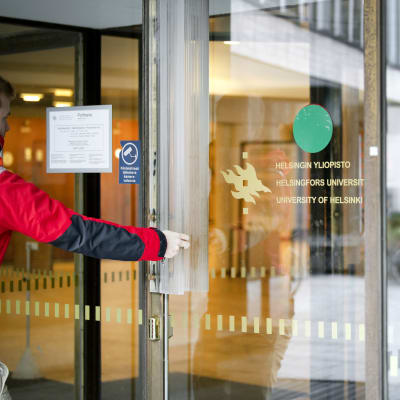 Person som håller på att gå igenom en glasdörr med texten Helsingfors universitet.