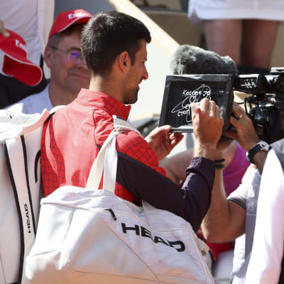 Novak Djokovic kirjoittaa kameran linssiin.