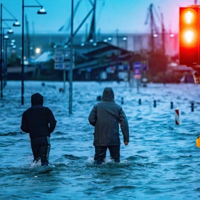 Kaksi ihmistä etenee veden valtaamalla kadulla.