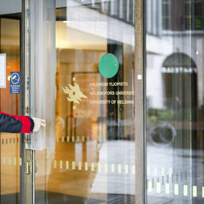 Person som håller på att gå igenom en glasdörr med texten Helsingfors universitet.