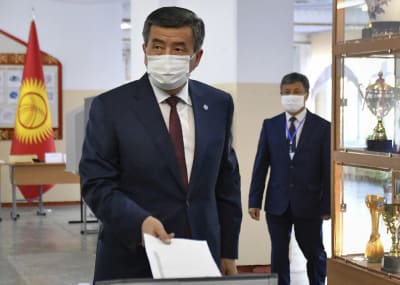 Sooronbai Jeenbekov pudottaa äänestyslipuketta vaaliuurnaan maski kasvoillaan