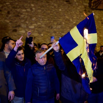 Mielenosoittajat polttavat Ruotsin lipun.