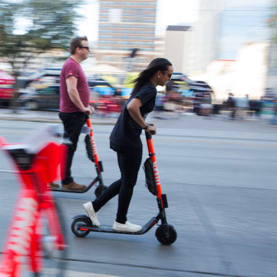 En man och en kvinna i Austin i Texas åker sparkcykel i riktning högerut på bilden. 