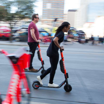 En man och en kvinna i Austin i Texas åker sparkcykel i riktning högerut på bilden. 
