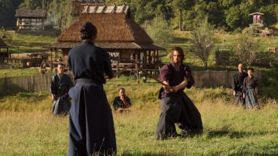 Två samurajklädda män står beredda att gå in i kamp med dragna svärd.