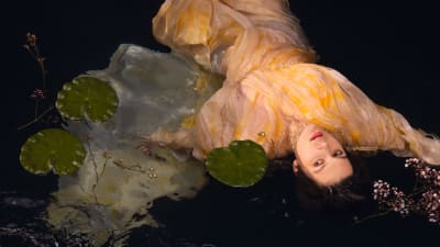 En mörkhårig kvinna som ligger i vattnet bland näckrosblad.