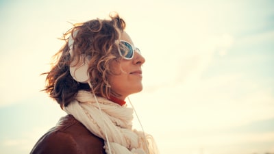 Kvinna i solglasögon har hörlurar på sig och lyssnar på musik.