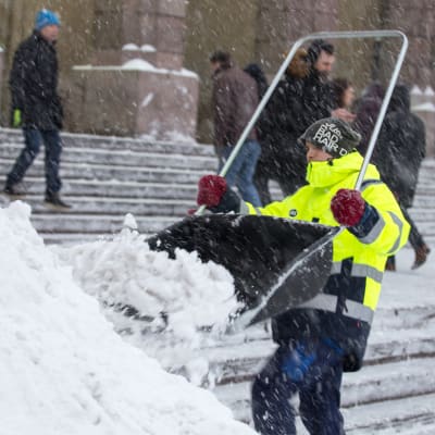 Mies heittää lunta lumikolalla Helsingin päärautatieasemalla.