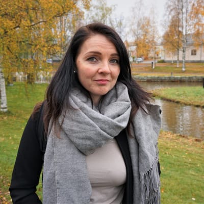 Kvinna i svart jacka står i en park.