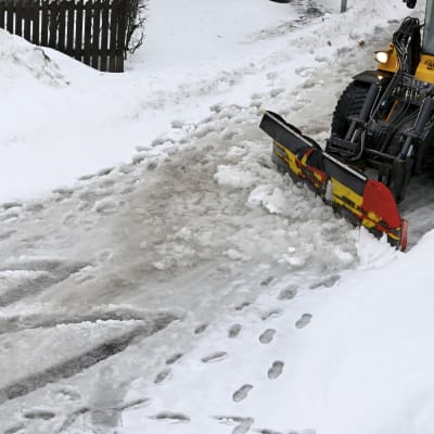 En person går på en snöslaskig gata som plogas.