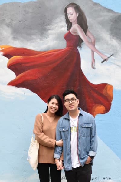 Ett par poserar framför en målad vägg i Hongkong. Målningen förekommer en kvinna som dansar.