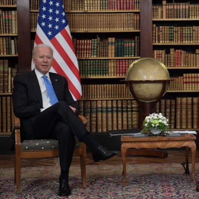 Joe Biden ja Vladimir Putin istuvat maidensa lippujen ja kirjahyllyn edessä.