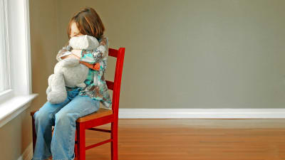 Ett ensamt barn kramar ett mjukisdjur. 