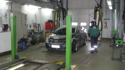 En mörkblå bil i en besiktningshall. Besiktningsmannen står bredvid med ryggen till.