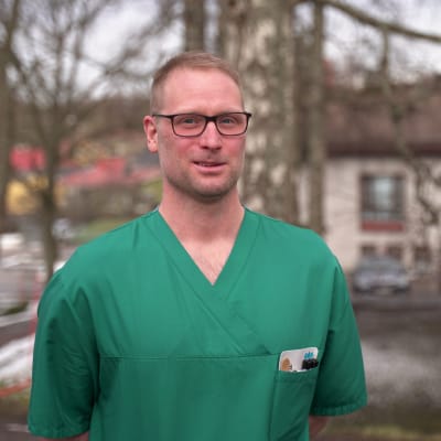 Man i 40-årsåldern med kort hår, glasögon, grön sjukskötarblus och vita byxor.