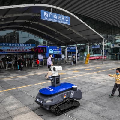 En polisrobot påminner människor om att de ska bära skyddsmask, och mäter febern på dem.  Shenzhen,  provinsen Guangdong 6.3.2020 