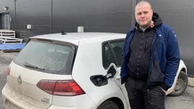 En man står intill sin vita bil med ett öppet tanklock. 