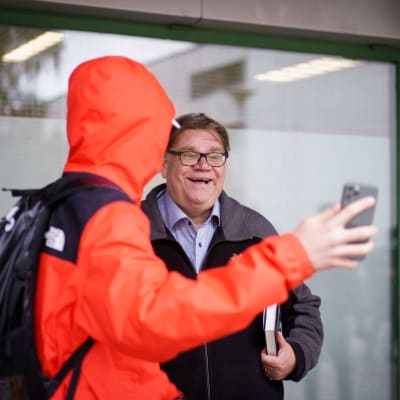 En ung person i orange jacka tar en selfie med Timo Soinin i ett köpcenter i Ivisnäs.
