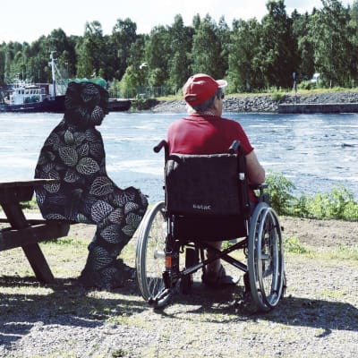En vårdare och en man i rullstol tittar ut över floden