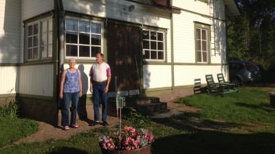 Ett medelålders par poserar framför ett vitt egnahemshus.