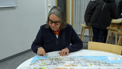 En kvinna sitter vid ett runt bord och studerar en karta.