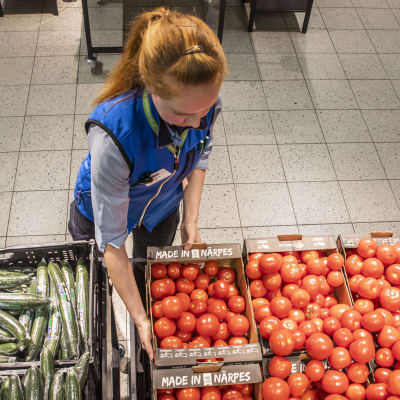 En ung kvinna fyller grönsakshylla i en affär
