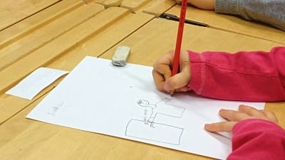 Flicka ritar på ett papper vid en pulpet